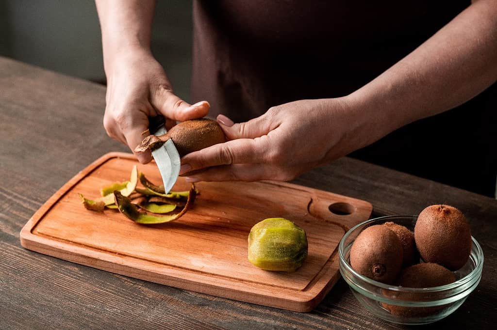 Carefully peeling fresh kiwi on wooden cutting board for nutritious dog treats.
