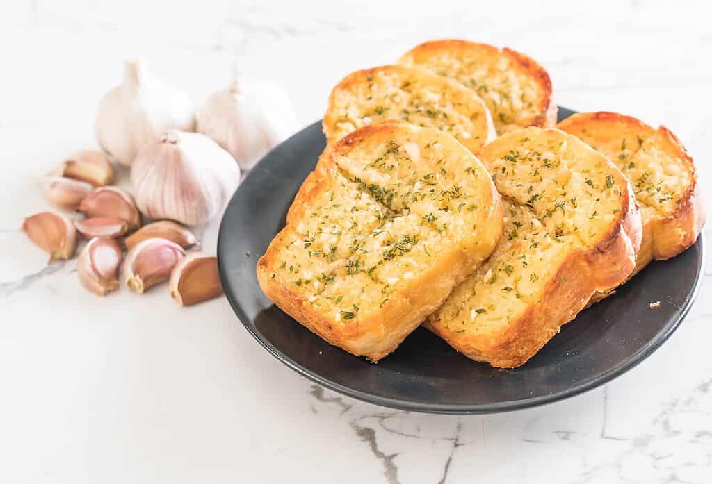 Delicious garlic bread slices topped with herbs and butter on a black plate. Perfect for a savory snack or side dish.