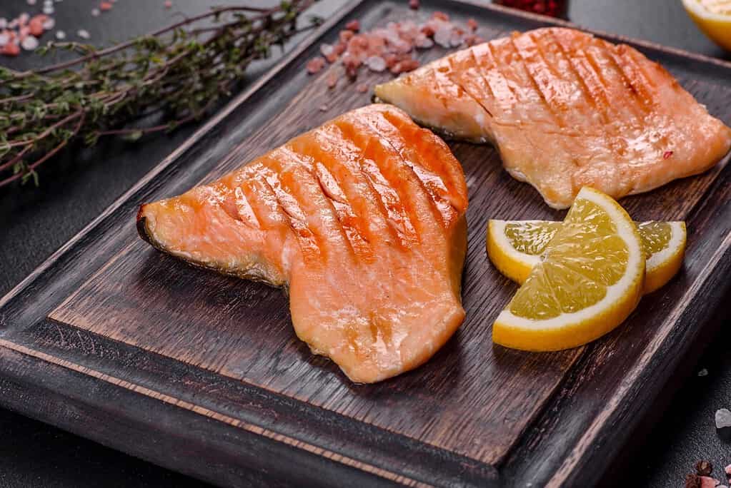 Fresh cooked salmon with lemon wedges on wooden board, healthy dog treat.