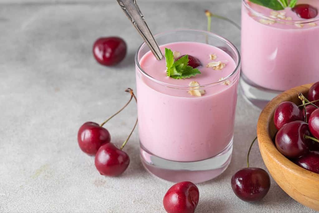 Delicious pink cherry yogurt smoothie in a glass with fresh cherries and mint, perfect for healthy summer refreshment.