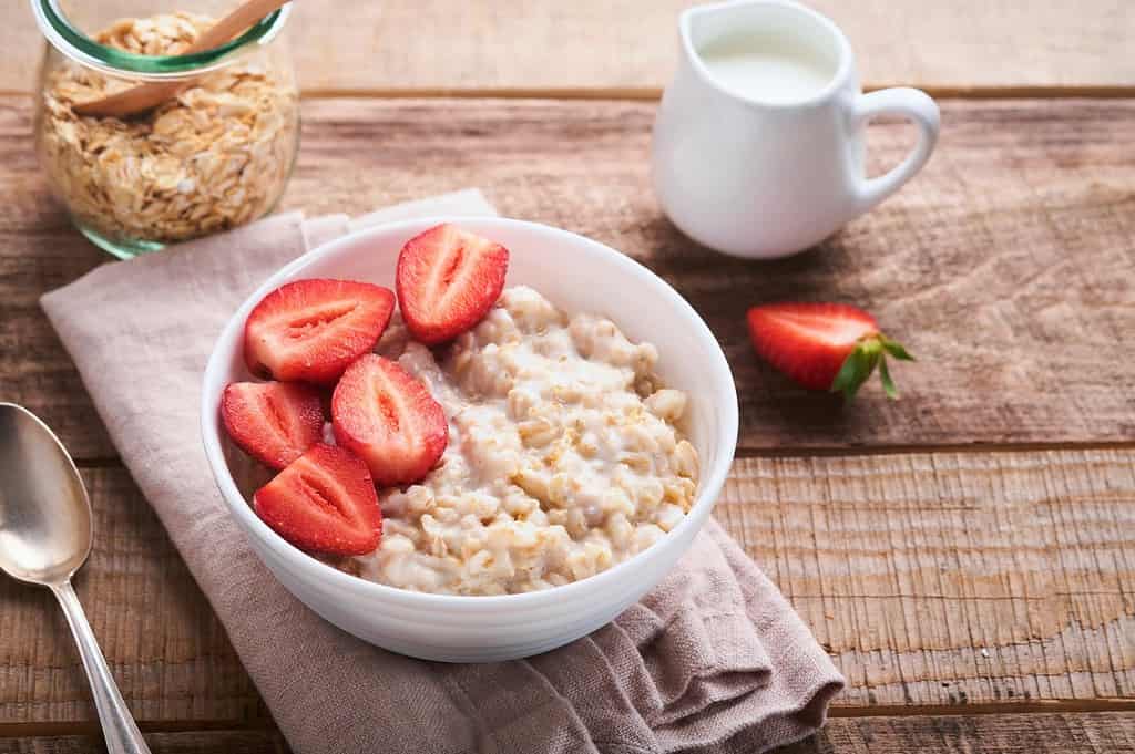 Bright strawberry oatmeal breakfast with fresh strawberries and milk in a white bowl.