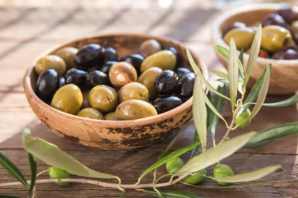 Organic black and green olives in wooden bowls on rustic table.