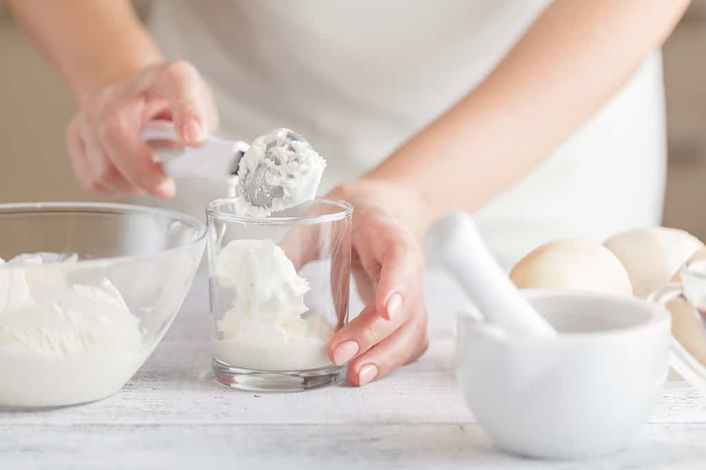 Alt text: Person scooping homemade ice cream into a glass, with bowls of ingredients on the table.