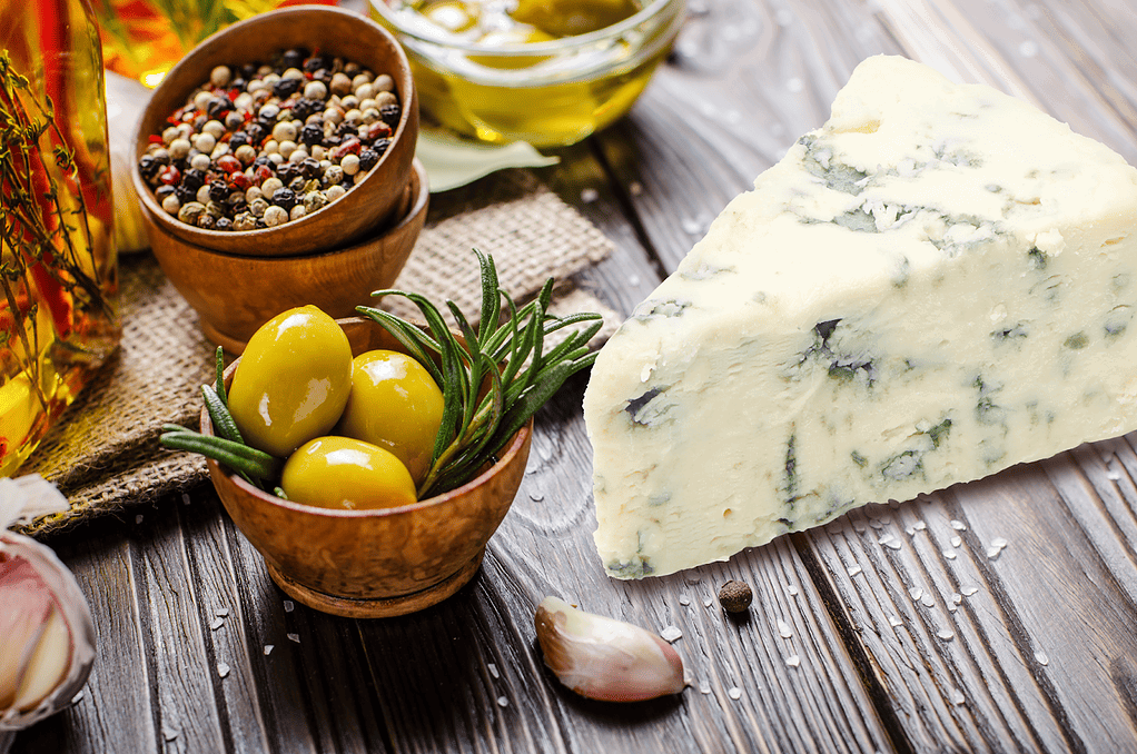 Delicious blue cheese accompanied by herbs, spices, and olive oil on a wooden table.