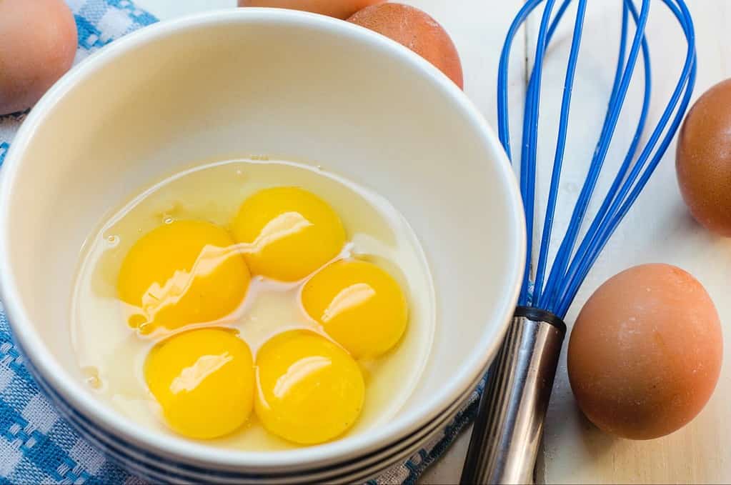 Bright yellow eggs in a white bowl on a kitchen counter.