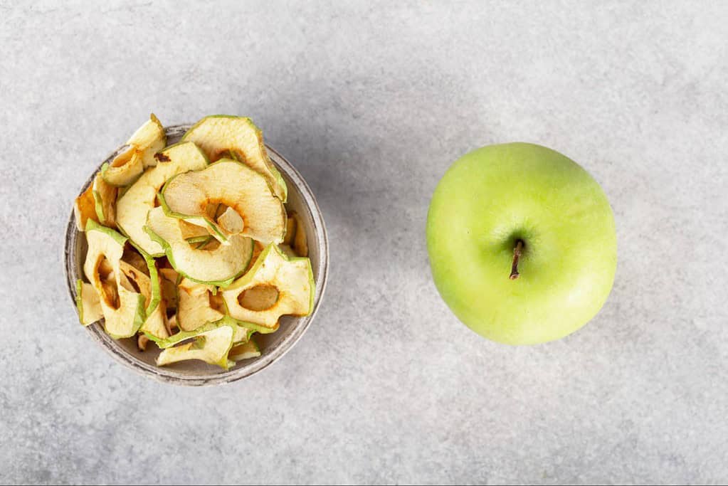 Bright green apple next to dried apple and zucchini dog treats.