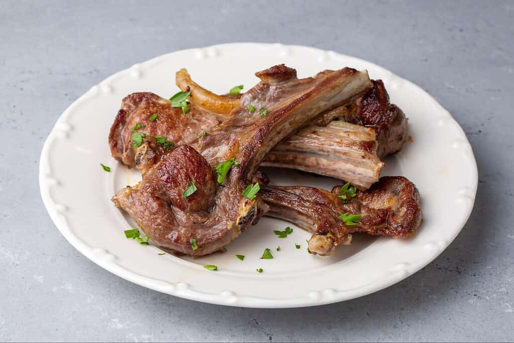 Delicious cooked lamb chops garnished with fresh herbs on a white plate. Perfect for dog-friendly, nutritious pet meals.