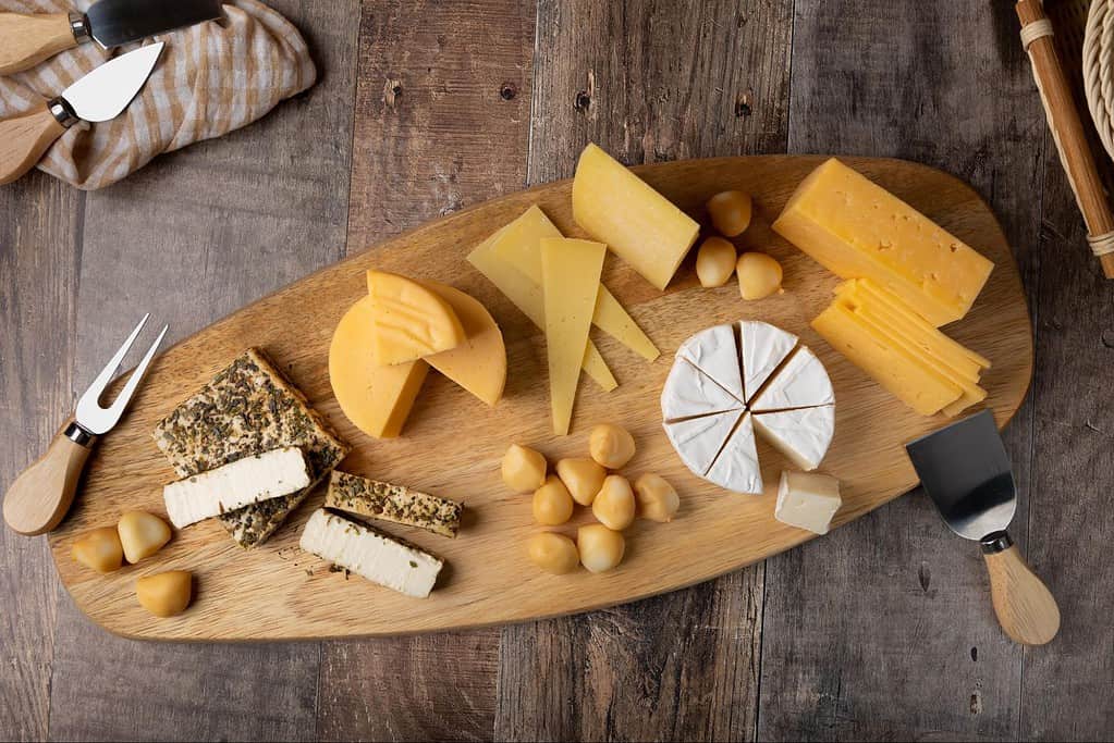 Varying cheese types including hard, soft, and blue cheese with nuts, served on a rustic wooden table.