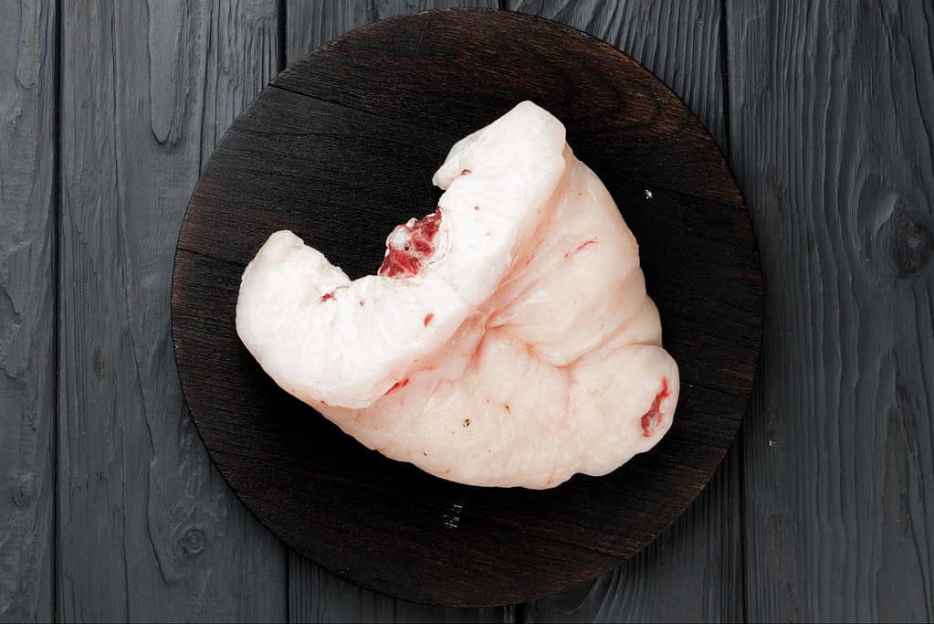 Raw pig fatback on a dark wooden platter for pet diet.