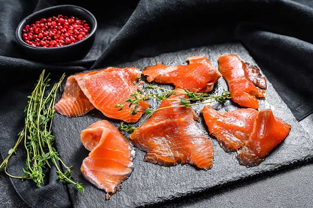 Fresh salmon slices with herbs on slate.