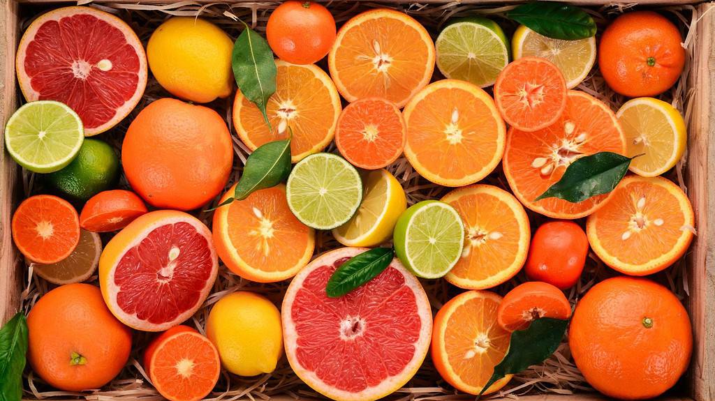 Colorful assorted citrus fruits including grapefruits, oranges, lemons, and limes with green leaves on a rustic wooden background.