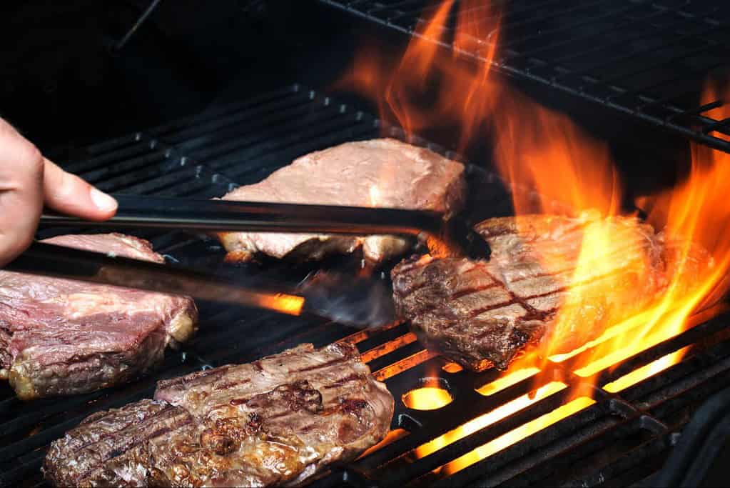 Close-up of delicious steaks being grilled over open flame on barbecue. Perfect for outdoor cooking and summer BBQs.