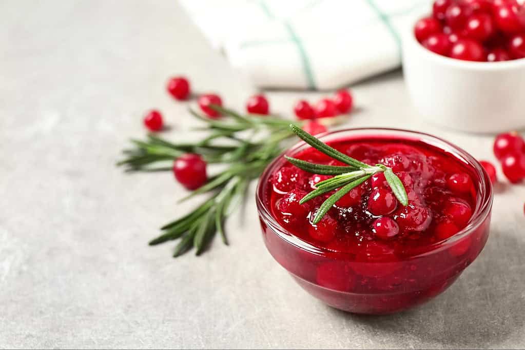 Fresh red berry jam in a glass bowl with rosemary garnish.