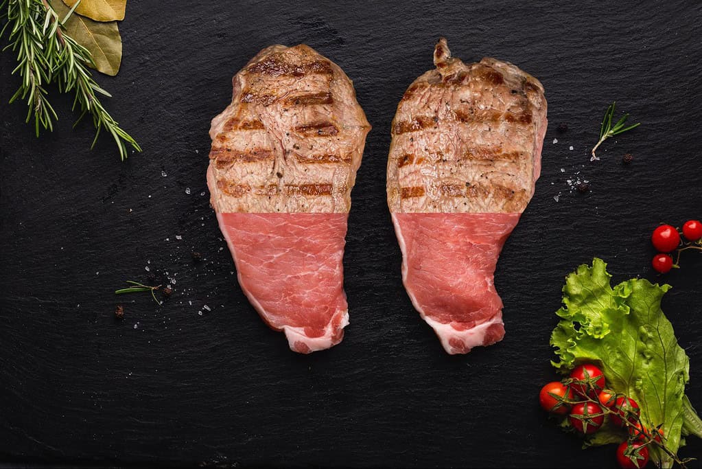 Juicy, grilled steak served with fresh herbs and cherry tomatoes on a dark slate board.