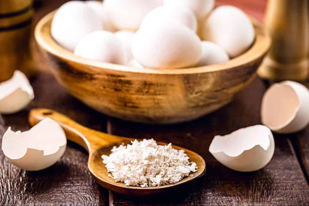 Fresh eggs in a wooden bowl with shells cracked open, ideal for baking or cooking recipes.