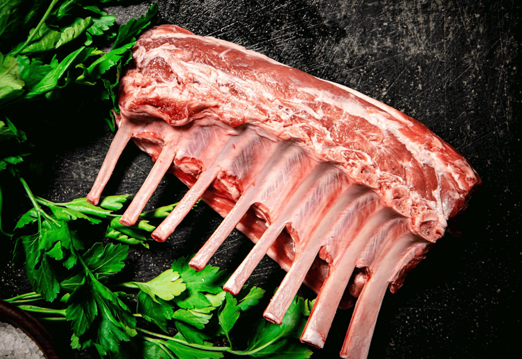Fresh raw lamb ribs with green herbs on black textured background.