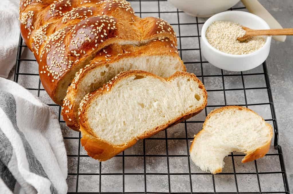 Delicious homemade bread loaf with sesame seeds, sliced for serving, shown on a cooling rack with bowl of sesame seeds.