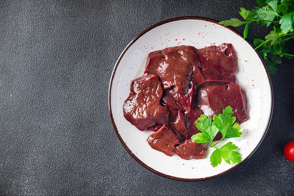 Dog-friendly raw liver meat on a white plate with fresh herbs, suitable for canine nutrition.