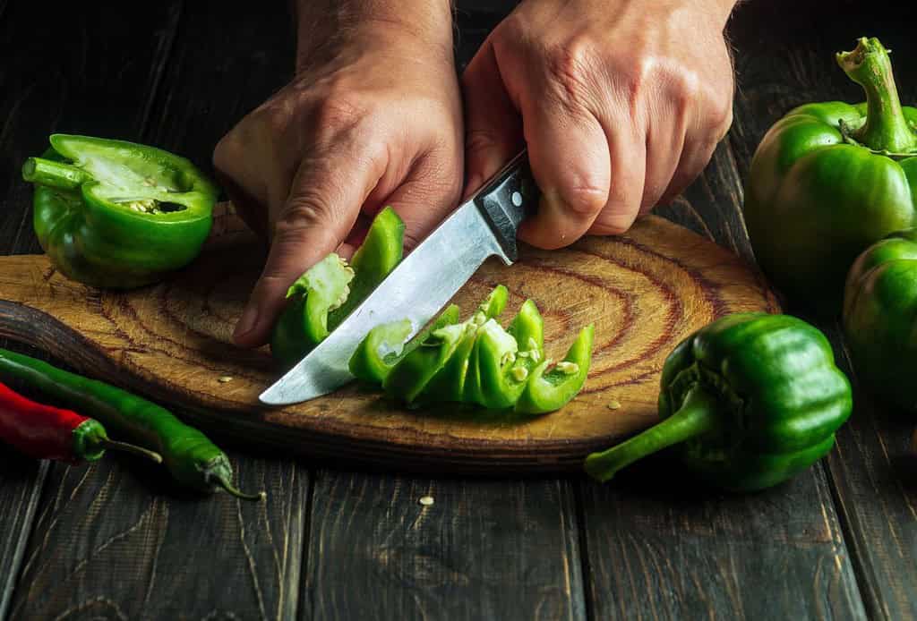 Close-up of hands slicing green peppers for nutritious homemade dog food.