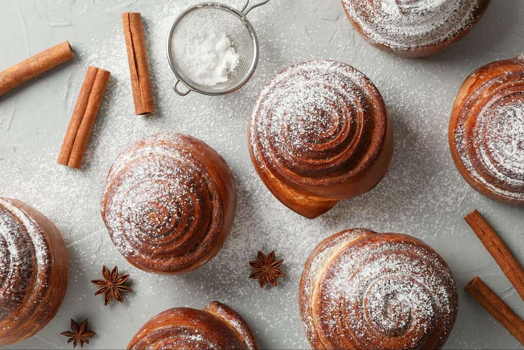 Delicious homemade cinnamon rolls topped with powdered sugar and cinnamon sticks, perfect for breakfast or treats.