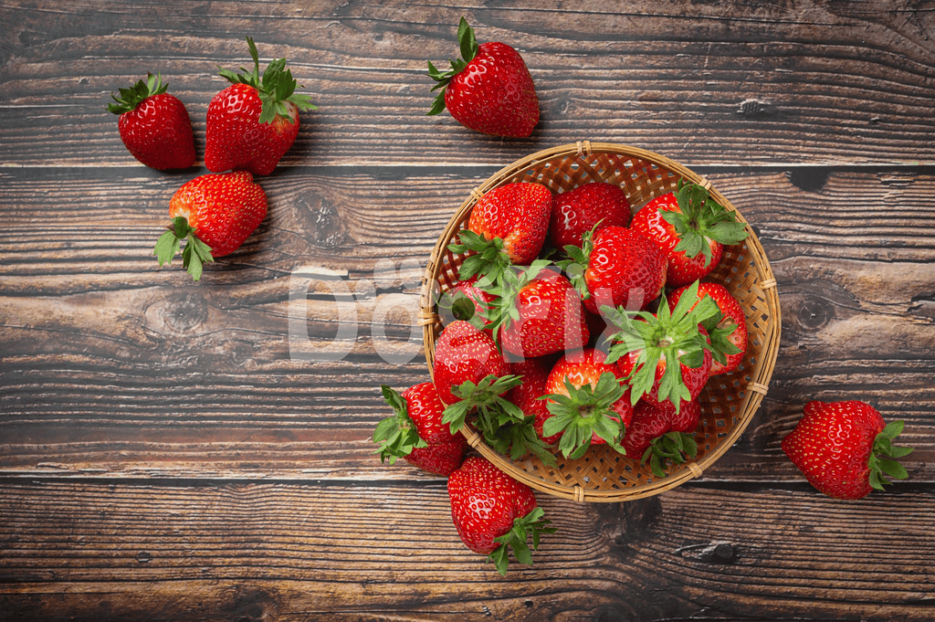 Bright red strawberries with green leaves in a wicker basket on rustic wooden table.
