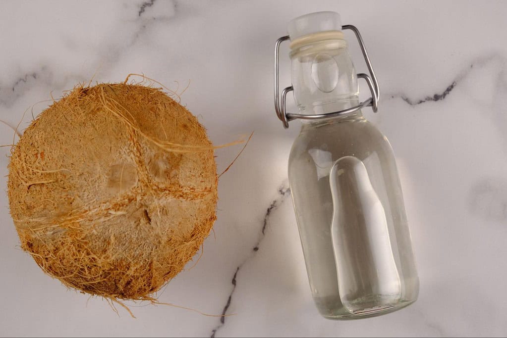 Natural coconut oil in a glass bottle with coconut halves on a white background.