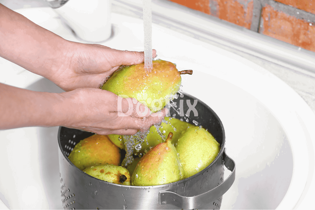 Hand washing fresh pears in a kitchen sink, preparing healthy dog treats with natural ingredients.