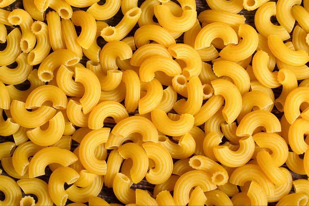 Vibrant yellow macaroni pasta scattered on a dark surface.