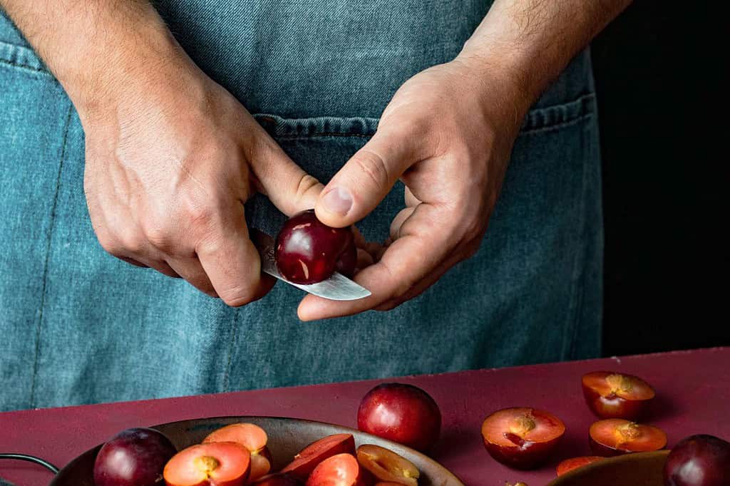 Close-up of person slicing cherries with a knife, emphasizing fresh fruit preparation for a healthy lifestyle.