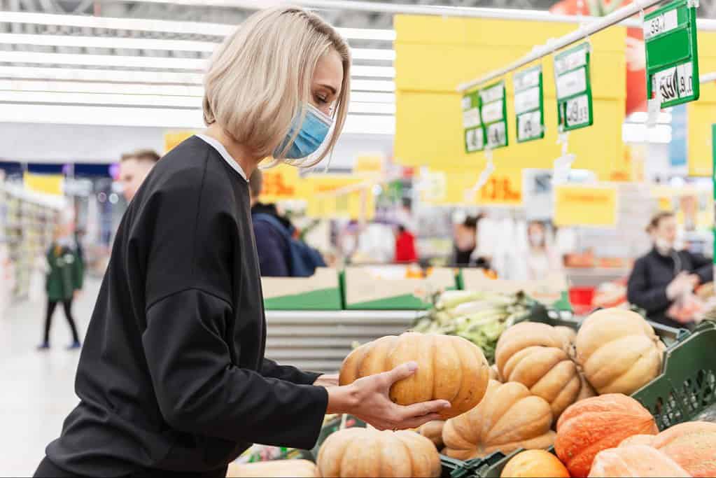 Woman wearing face mask selecting pumpkins at supermarket for pet-friendly autumn recipes.
