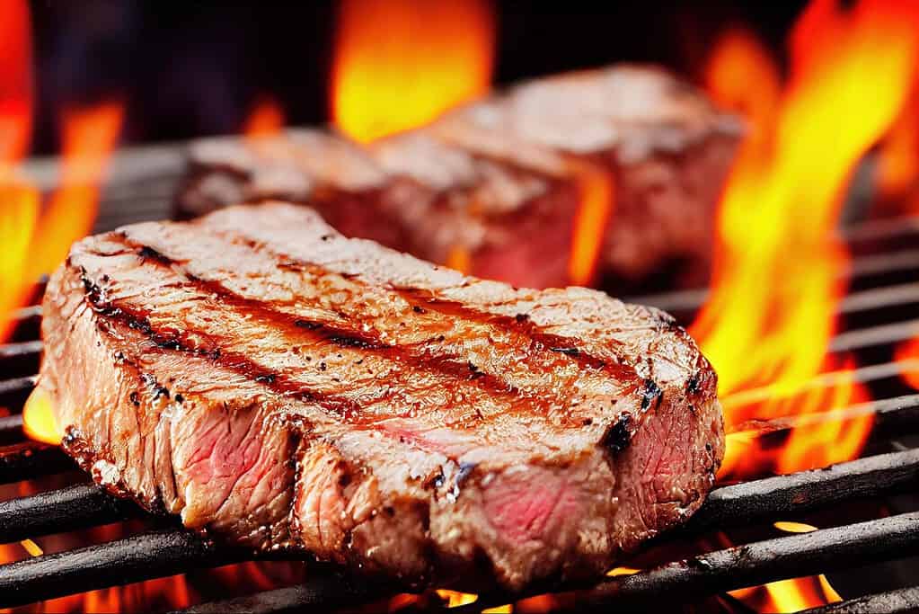 Juicy grilled steak on open flame with grill marks, ideal for barbecue and grilling recipes.