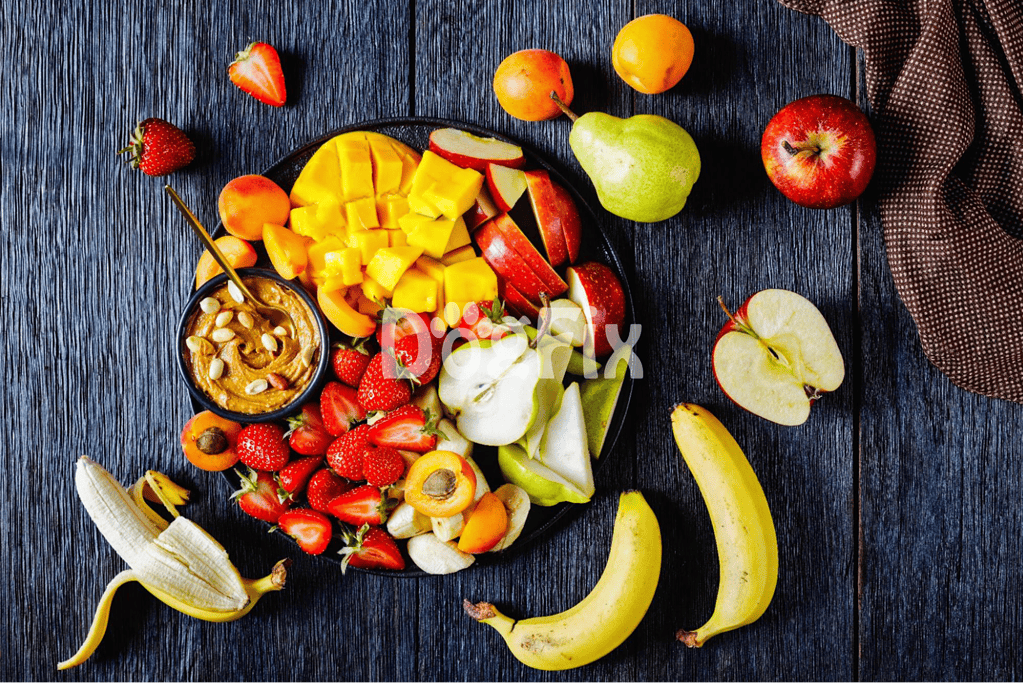 Colorful assortment of fresh fruits including strawberries, apples, bananas, mango, and pears on dark wooden surface.