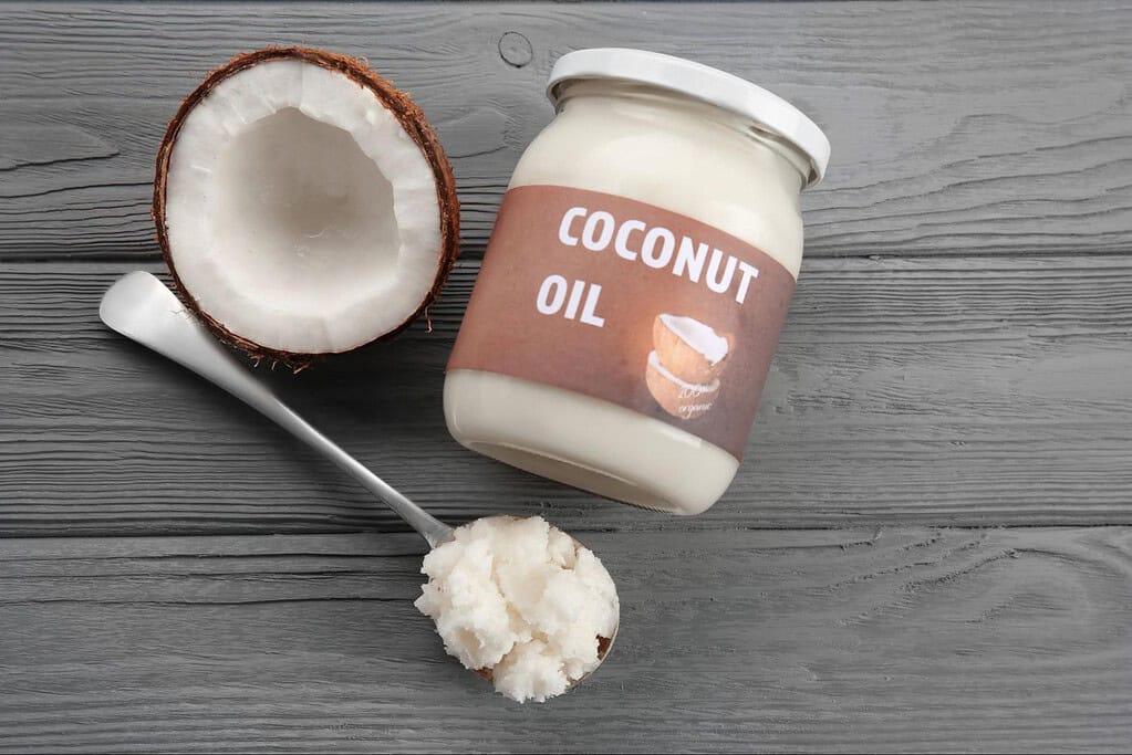 Natural coconut oil in a glass bottle with coconut halves on a white background.