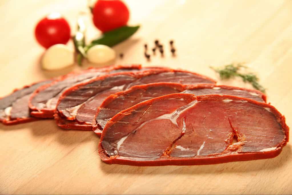 Tasty assorted meat slices including beef, turkey, and ham with herbs and vegetables on a wooden background.