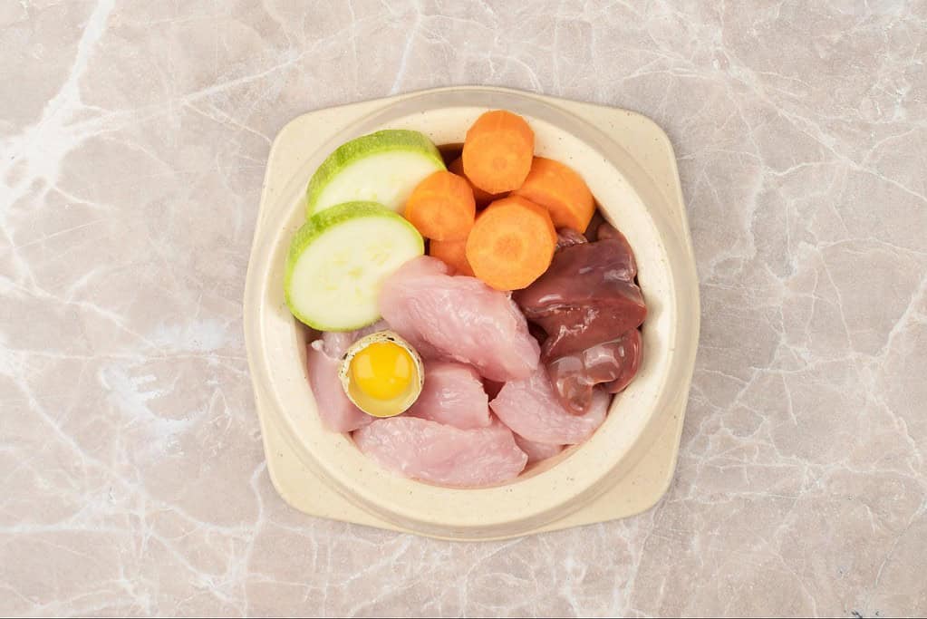 Healthy dog food ingredients: chicken, liver, egg, cucumber, carrots for nutritious pet meals.