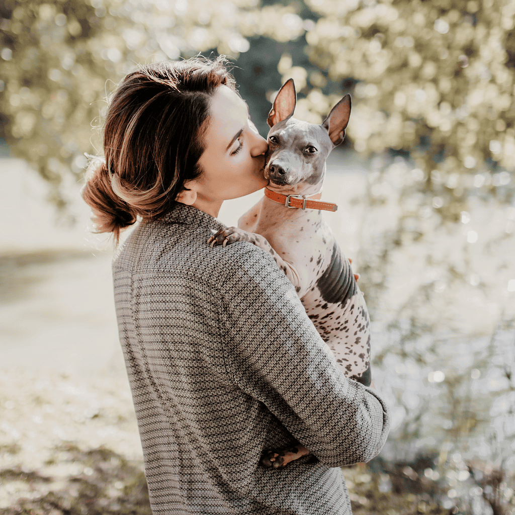 Adorable woman kissing her playful Australian Terrier outdoors, capturing love and bond with pet.