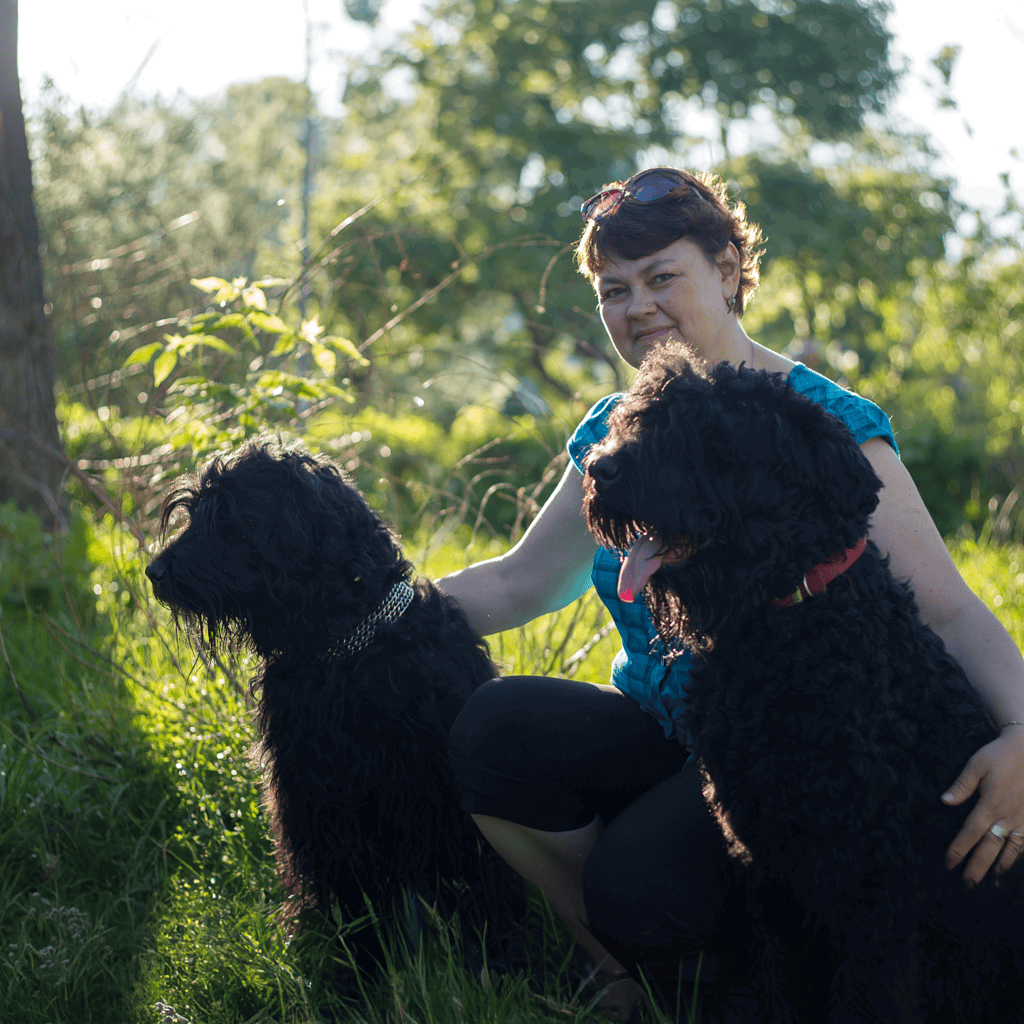 Friendly woman playing with her two large black dogs in a green outdoor setting.
