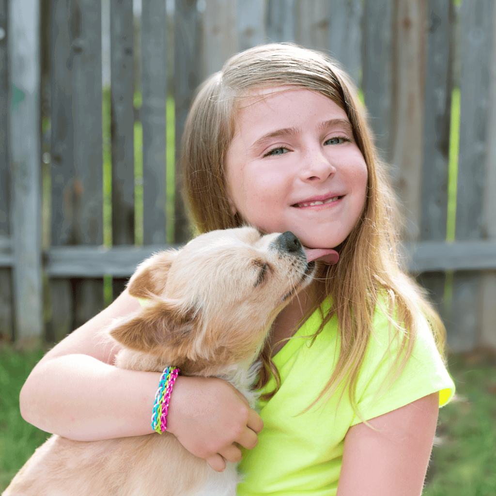 Adorable girl hugging puppy outdoors, smiling with affection, wooden fence background, joyful pet bonding.