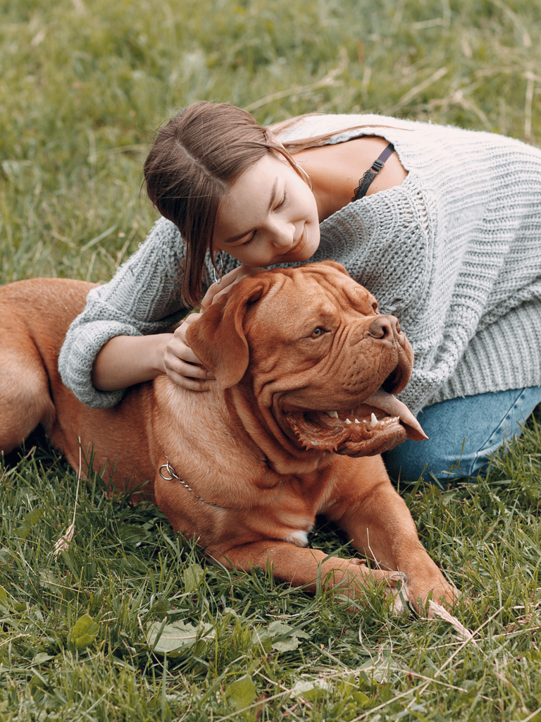 Adorable woman cuddling her large brown dog on a grassy field.