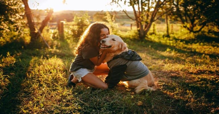 Girl cuddling her golden retriever in a sunny outdoor setting during golden hour.
