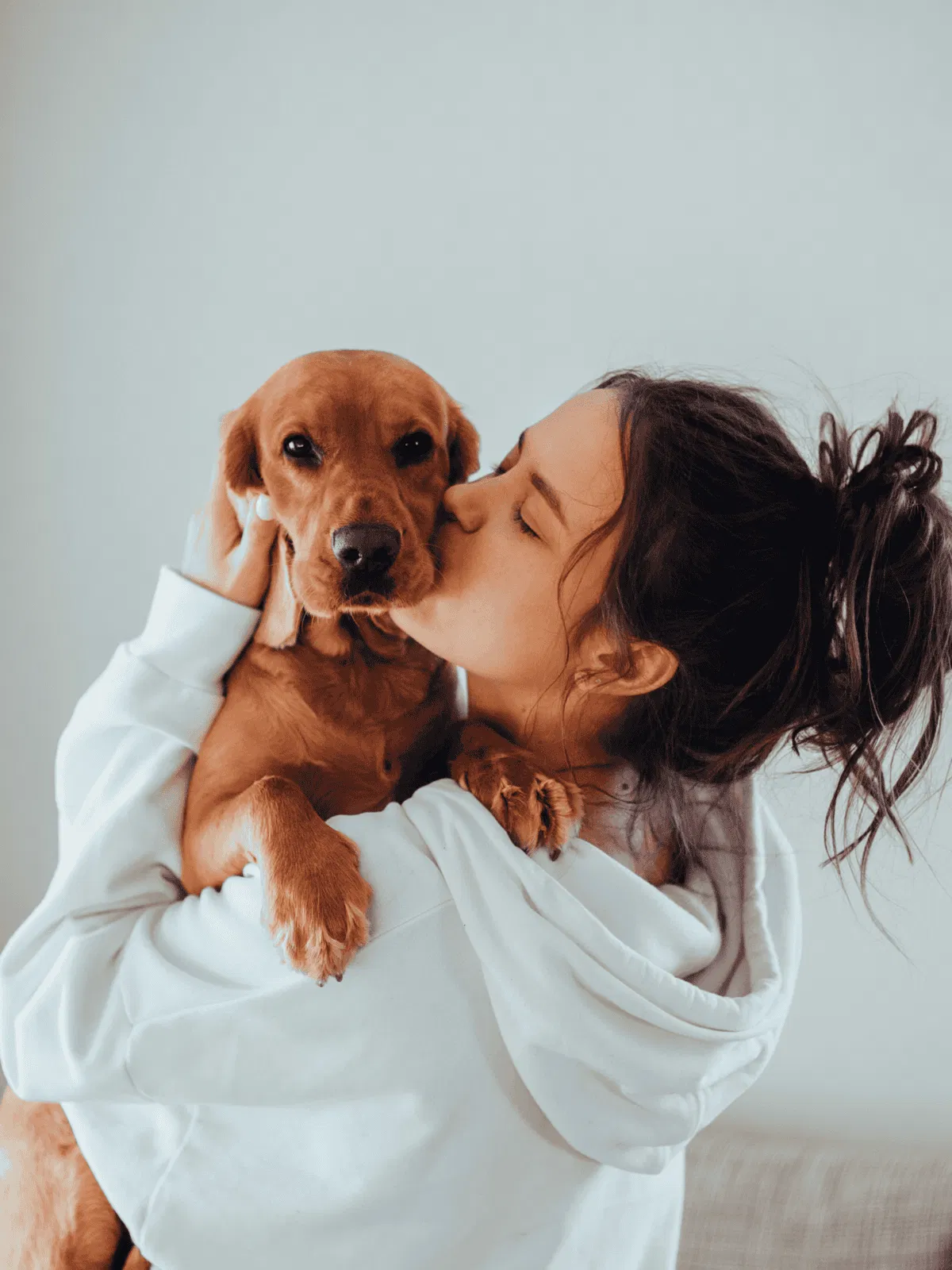 Adorable woman cuddling her cute brown dog in a cozy white hoodie.