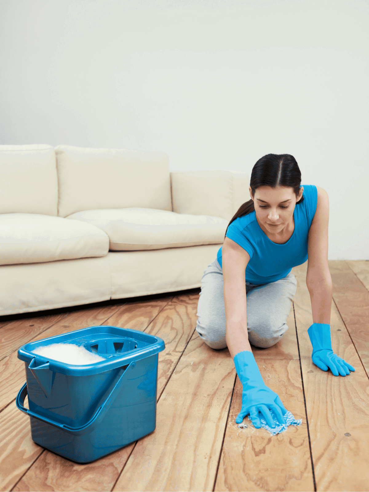 Woman in blue gloves cleaning hardwood floor with mop and bucket.