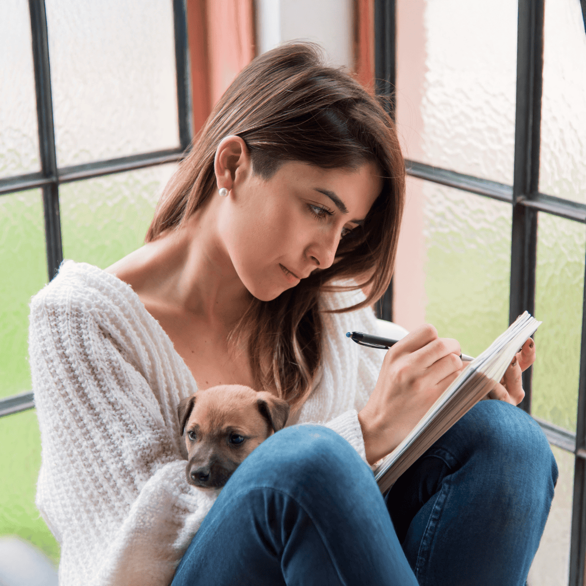 Woman with a puppy, sitting by the window, journaling or working on a project peacefully.