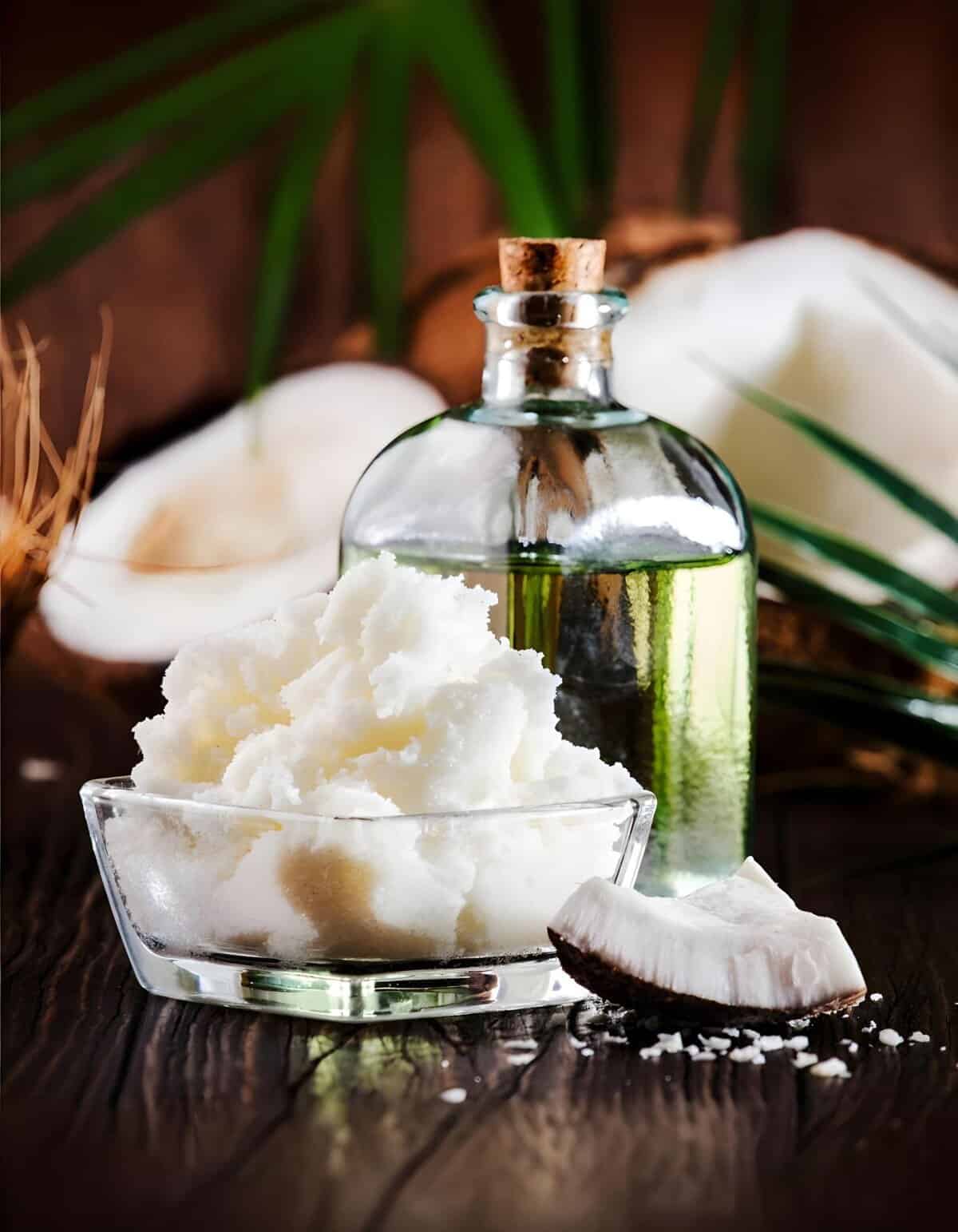All-natural coconut oil in a glass bottle with a bowl of shredded coconut and coconut pieces.