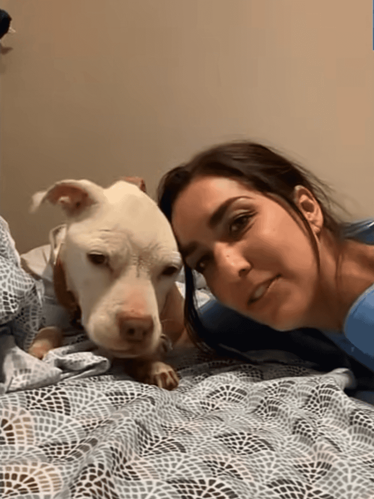 Dog and woman lying on bed together, smiling.