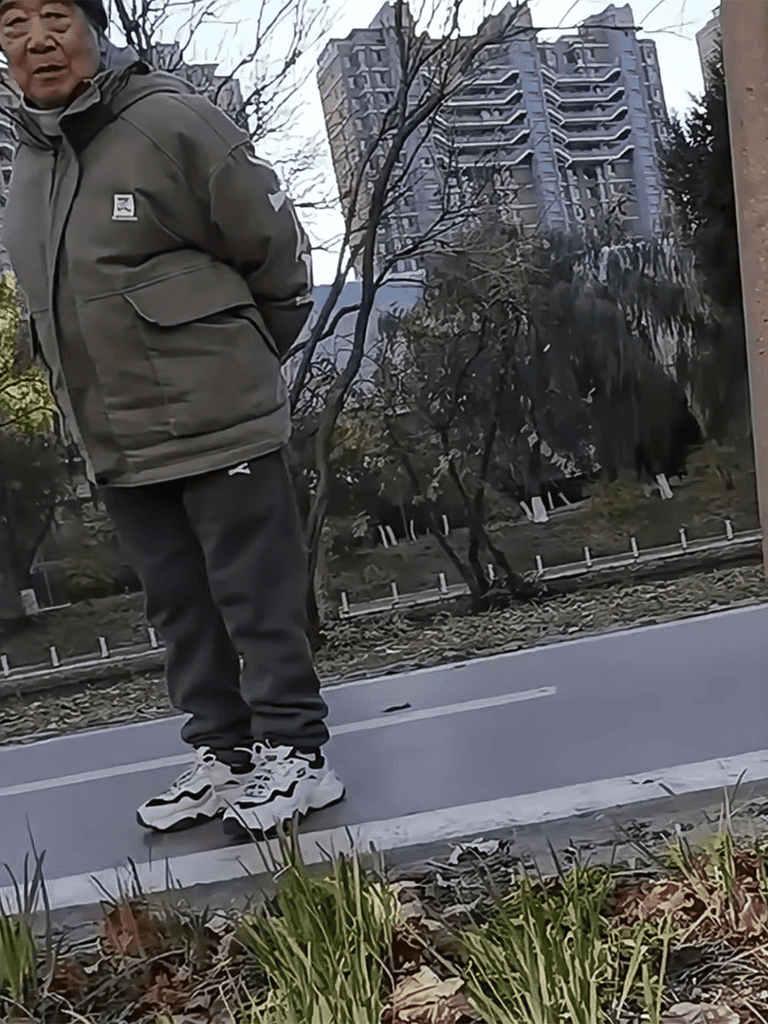 Man in casual streetwear on city sidewalk, urban background with buildings and trees.