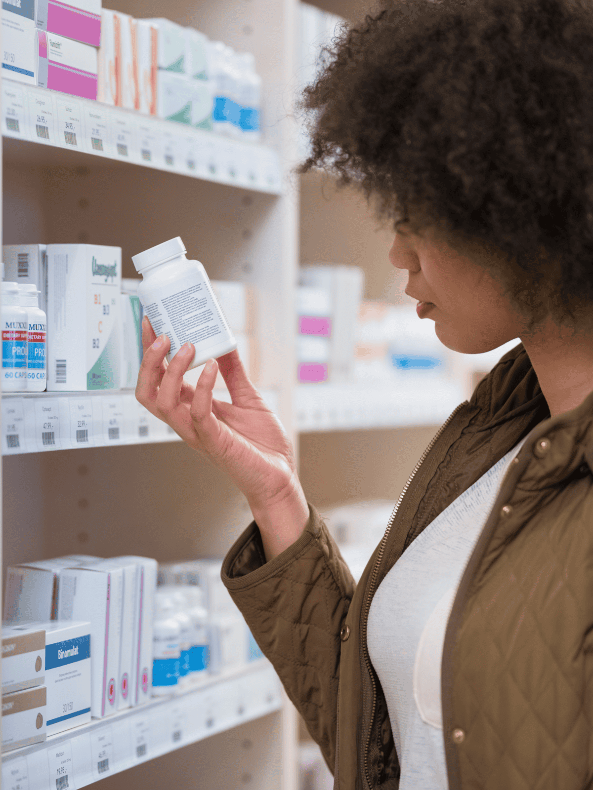 A woman selecting medication from a pharmacy shelf.