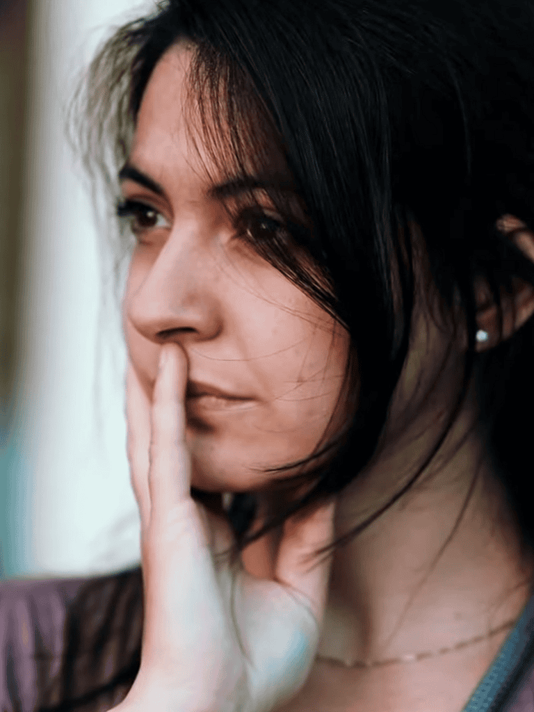 Close-up of a woman with dark hair holding her finger to her lips, contemplating or being silent.