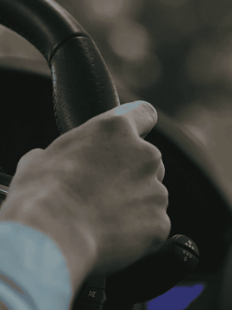 Close-up of a person's hand gripping a car steering wheel, emphasizing safe driving and road safety.