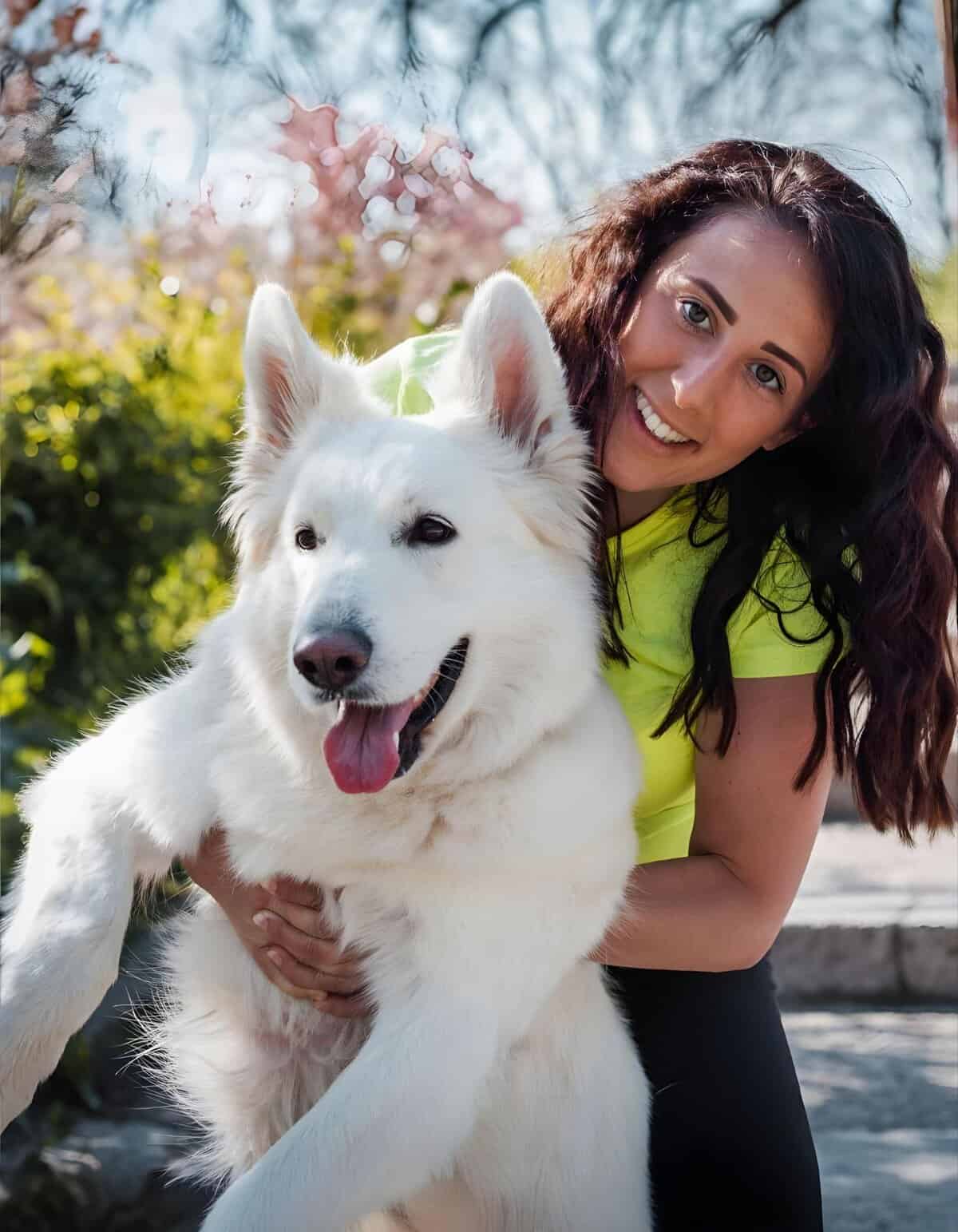 Adorable woman with white Siberian Husky in blooming garden on sunny spring day.